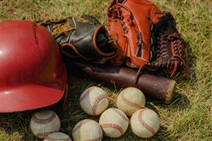 Well-used softball mitt, bat, helmet, and balls piled on the grass.